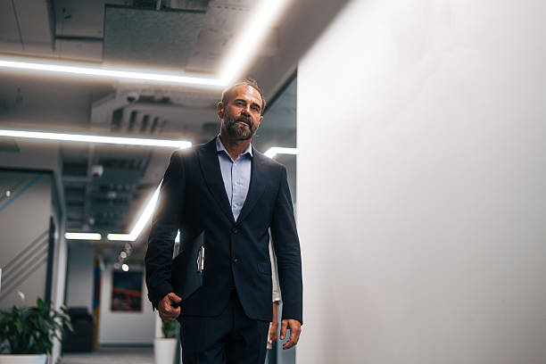 istock Mature businessman walking office corridor holding clipboard 2245109675