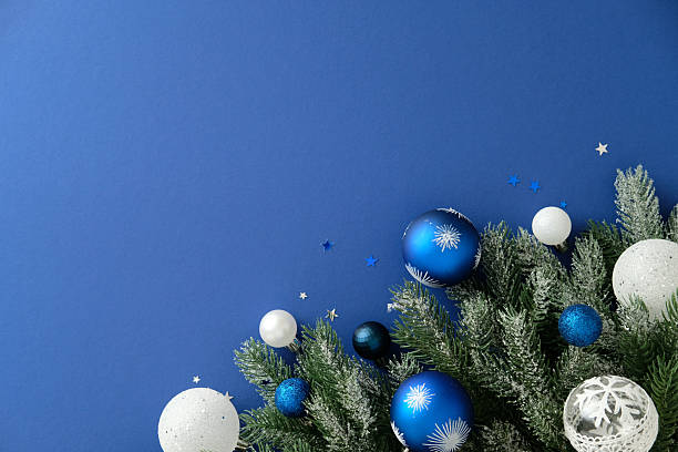 istock Christmas flat lay with blue, white, and silver baubles on frosted pine branches over blue background, decorated with star confetti for festive winter mood. 2245118041