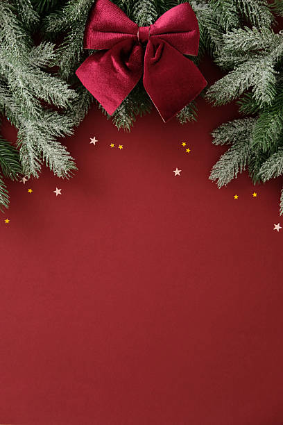 istock Snow dusted pine branches with burgundy velvet bow on deep red background. Christmas vertical banner design, New Year poster template. 2245118140