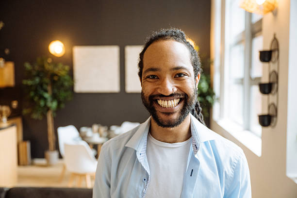 Smiling black man with a beard sitting on a dark sofa with surrounded by indoor plants and soft lighting
