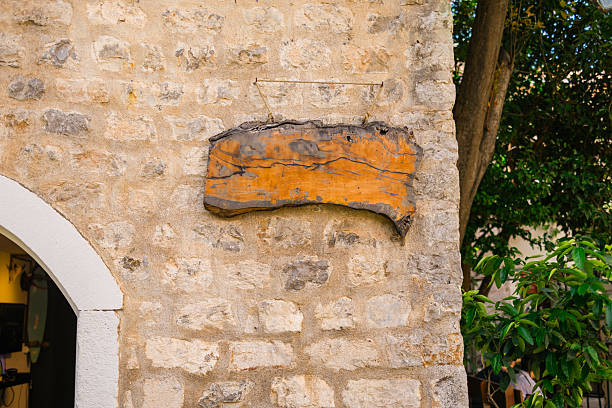 istock Blank rustic wooden sign hanging on stone wall outside a building. Vintage texture, handmade aesthetic, and space for custom text. 2245120859