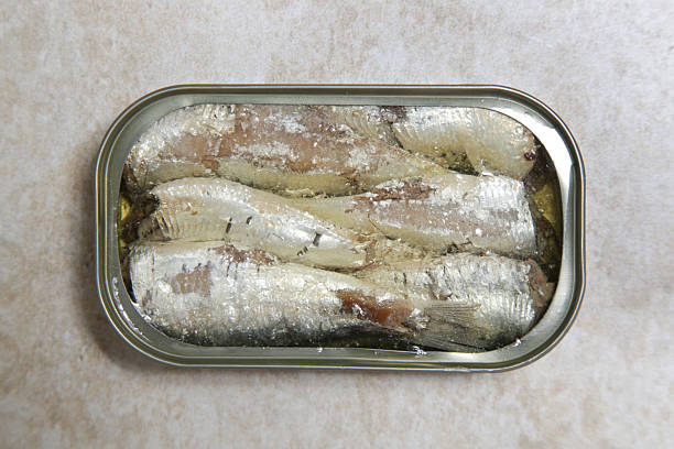 Tin can with tasty sprats with a wooden fork on a wooden table