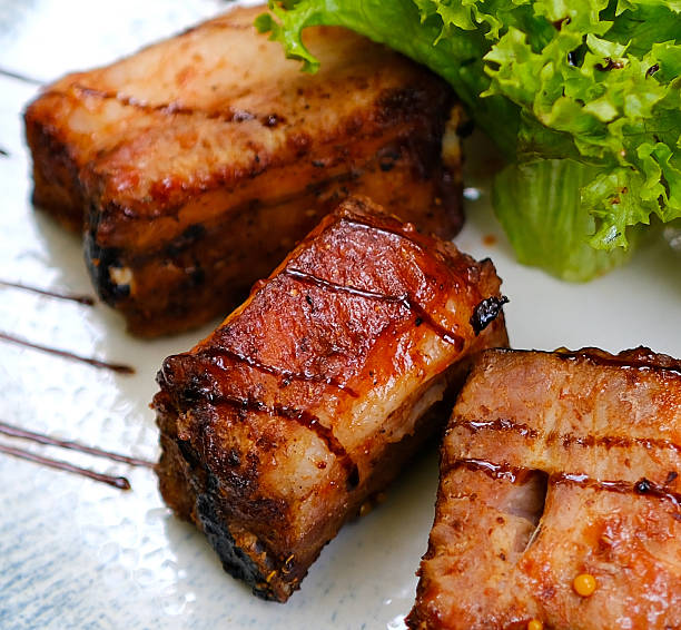 grilled pork ribs served with roast new potatoes on a white plate on a wooden table, horizontal view from above