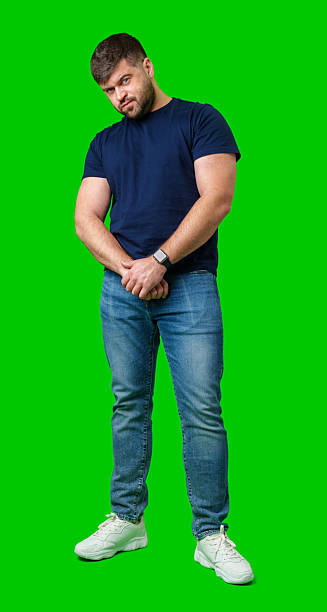 istock Man standing with a thoughtful expression in a casual outfit against a green background 2245127883