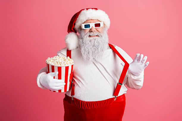 istock Santa with popcorn bucket and festive accessories strikes a playful pose in a pink studio background for Christmas 2245131384