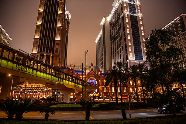 Taipa, Macau on 10 JANUARY 2024. The Venetian Macao's stunning facade under a cloudy sky, framed by lush trees at night. A grand Venetian-style building with a tall clock tower, creates a captivating scene.