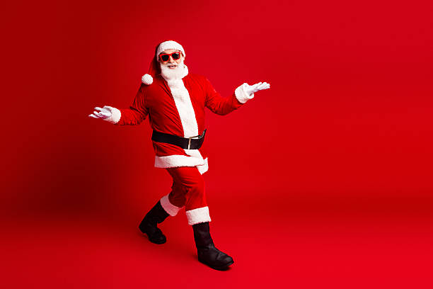 istock Santa in a red costume with hat belt and sunglasses dances in a bold red studio background for festive Christmas and holiday stock image 2245134747