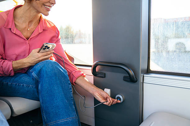 Woman riding a public transit bus, plugging in a usb cable to charge her mobile phone, using modern city transportation