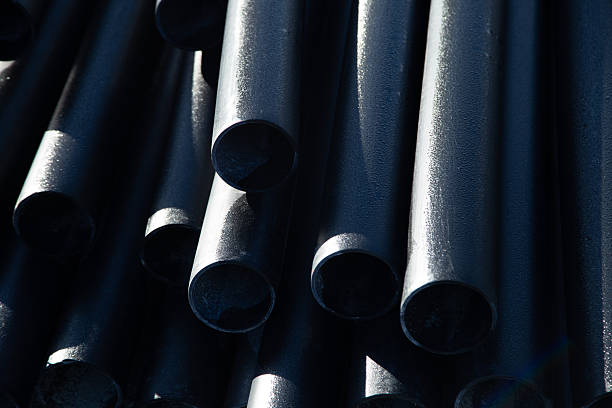 Stacked black pipes with a glossy finish accentuate industrial materials and textures, creating a visually striking composition in a production environment.