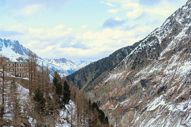 Alpen mountain valley with building and snow covered peaks under cloudy sky