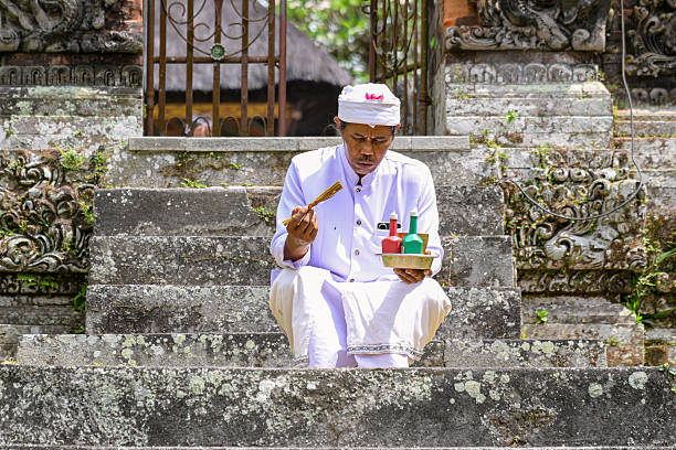 MENGWI, BALI, INDONESIA - MAY 13, 2025: Traditionally dressed unidentified Hindu religious people sitting on the floor and praying with their folded hands at Pura Taman Ayun Temple