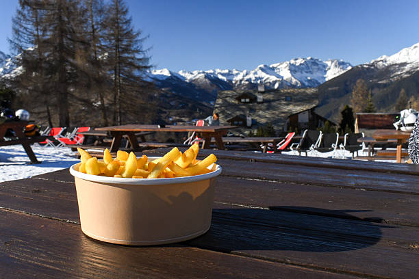 Delicious hot potato chips with a snowy mountain view. Outdoor lunch in a sunny European ski resort in winter. Fresh, golden french fries overlooking an Italian alpine valley in Sauze D'Oulx.