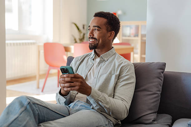 istock African American man sitting on a sofa using a smartphone in a modern home interior 2245156502