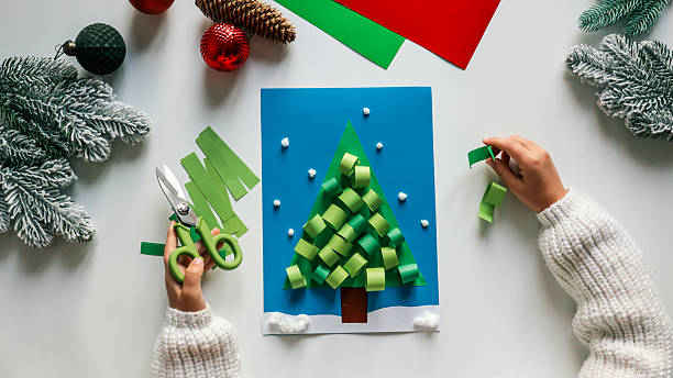 istock Child's handmade Christmas tree craft with paper and scissors on a white table 2245156985