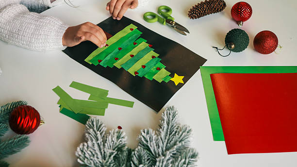 istock Child making a Christmas tree craft with paper and decorations on a white table 2245157005