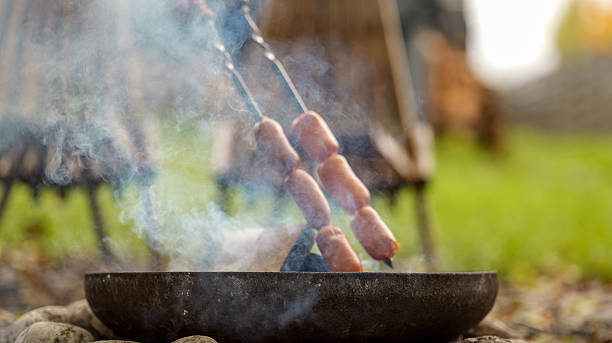 Sausages grilling over a fire pit with smoke rising into the air