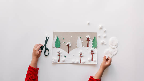 istock Child's winter art project with paper trees, cotton, and scissors on white background 2245159614
