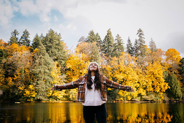 A Hispanic woman enjoys the big leaf maple trees and their fall colors in Washington state.  She walks through a wooded area, wearing a cozy sweater and hat.