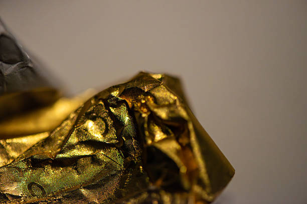 A detailed macro photo of a golden-colored shining chocolate wrapper, capturing texture, light reflection, and luxurious appeal.