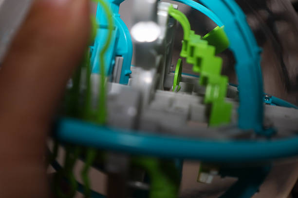 This blurred close-up focuses on the internal structure of a plastic 3D maze puzzle within a transparent sphere, showcasing intricate, interwoven tracks in lime green, turquoise, and gray.