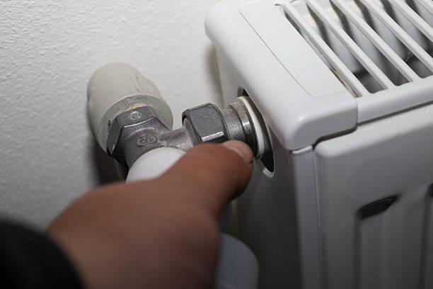 istock This close-up shot shows a human hand adjusting a thermostatic valve on a white heating radiator, emphasizing the importance of heat control and energy saving. 2245168221