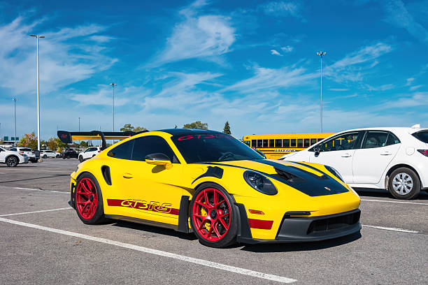 A yellow colored Porsche 911 GT3 RS high-performance sports car is parked in a parking lot in Montreal, Quebec, Canada, on a sunny day.