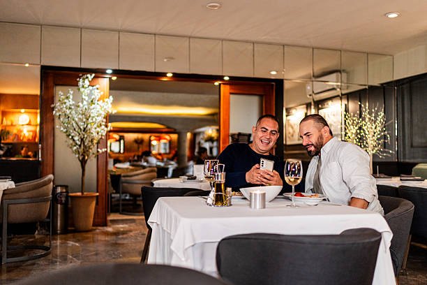istock Gay couple talking and using mobile phone during dinner at restaurant 2245176132