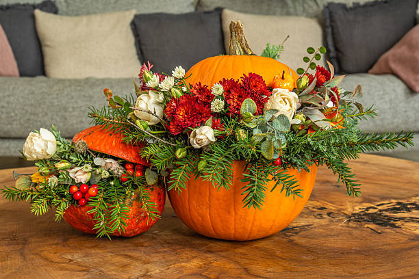 Two pumpkins transformed into elegant autumn vases, filled with white and red roses, chrysanthemums, berries, and evergreen branches. Set on a wooden table in a cozy indoor setting, these floral arrangements blend rustic charm with seasonal beauty.