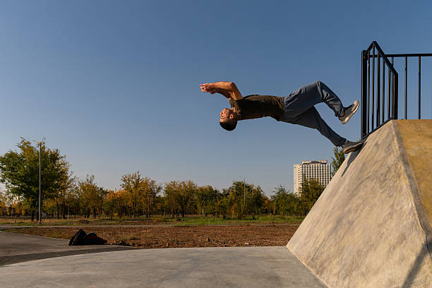 Male freerunner launches backward into a backflip from a sloped concrete wall during outdoor parkour practice in a park, showing athletic energy, motion, and advanced physical technique.