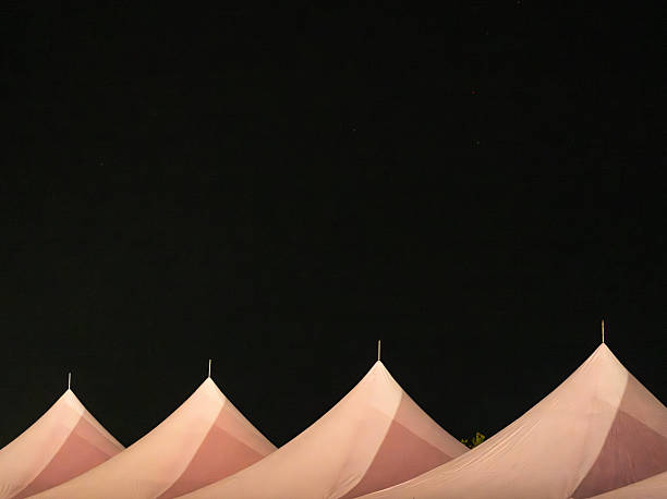 Three tent tops are silhouetted against a deep black night sky, creating a striking contrast with their pointed peaks.