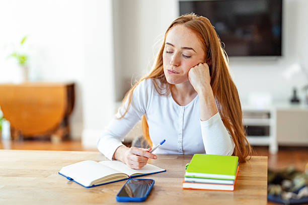Young woman studying thoughtfully at a table with notepad and smartphone in a bright, modern room
