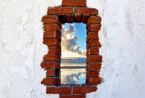 istock A rough brick window in a white wall frames a view of the beach with waves clouds and sky reflected in water at sunset creating a striking contrast between nature and structure 2245186456