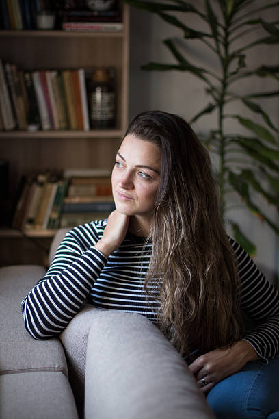 istock Young woman sitting by the window, relaxing on her couch. 2245190099