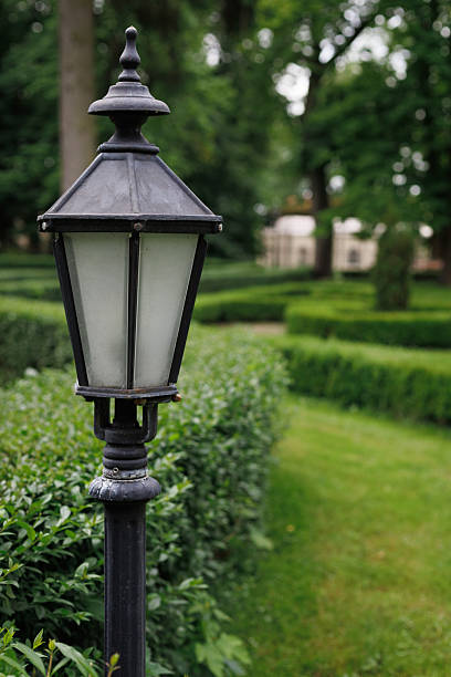 Old metal lamp surrounded by trimmed hedges and trees on a summer day. Detail of historical garden design.
