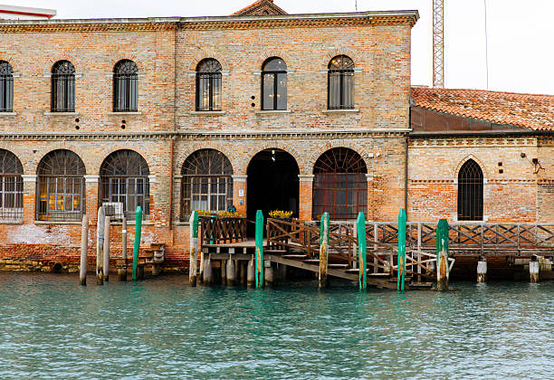 Murano, Italy - November 21, 2024: Historic building in Murano features brick facade and arched windows, reflecting on the serene water, capturing the island's unique charm