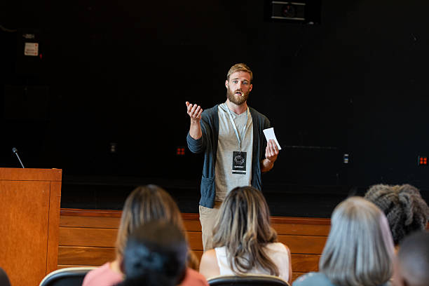 istock Speaker gesturing and holding notes addresses audience in auditorium 2245192483