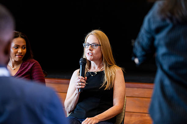 istock Woman speaking into microphone during discussion with people present in audience 2245192503