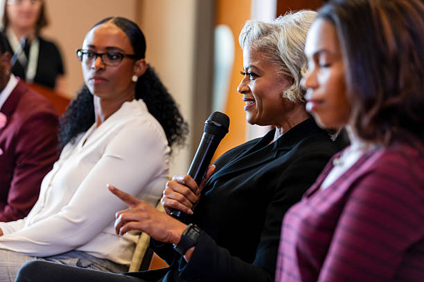istock A confident woman speaks into a microphone during a panel discussion, engaging the audience. 2245193691