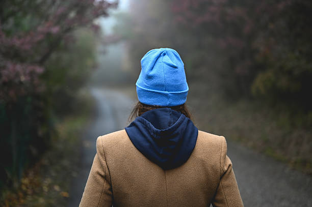 Young woman walking away into foggy nature, exploring a lonely journey