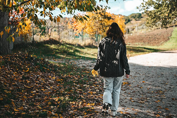 Woman walking along rural path with colorful fall leaves on a sunny autumn day