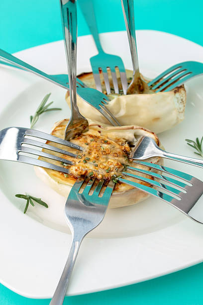 Roasted white eggplant on a white plate on a vibrant blue background with forks stuck in it. Creative composition of contemporary food