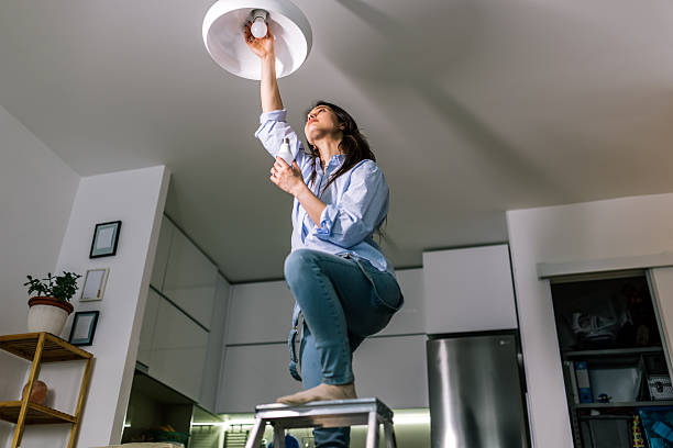 istock Young Woman Replacing Light Bulb in Chandelier 2245198533