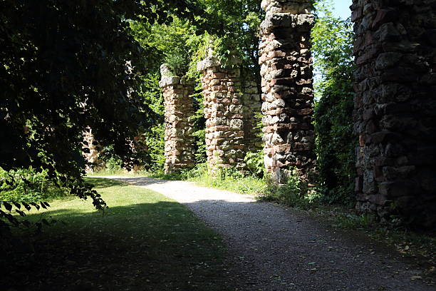 A scenic view of ancient stone arches covered with green vegetation in a peaceful summer park. The sunlight filters through the trees creating a play of light and shadow on the path. The image conveys calmness history and natural harmony making it ideal for illustrating travel heritage architecture and nature conservation concepts.