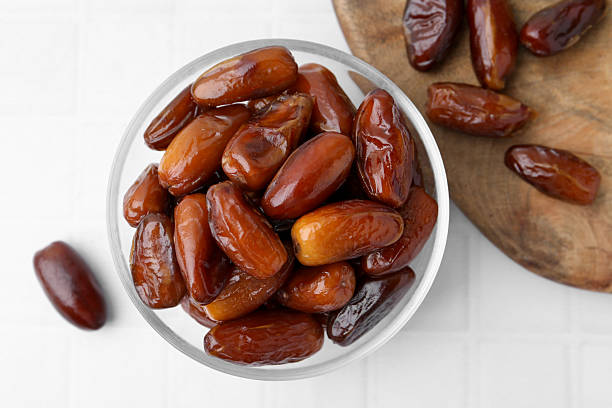 istock Tasty dried dates in glass bowl on white table, top view 2245207843