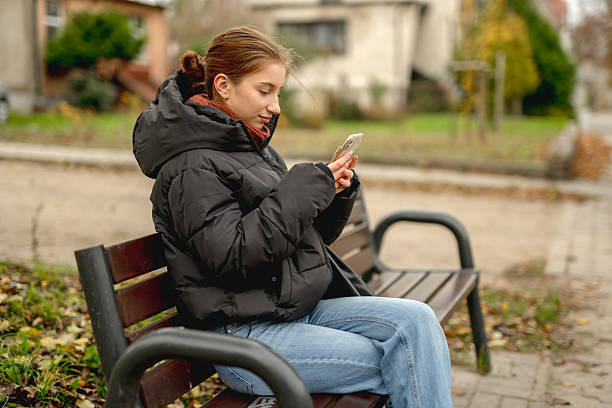 istock Sweet Girl Scrolling Phone While Sitting On Bench 2245208070