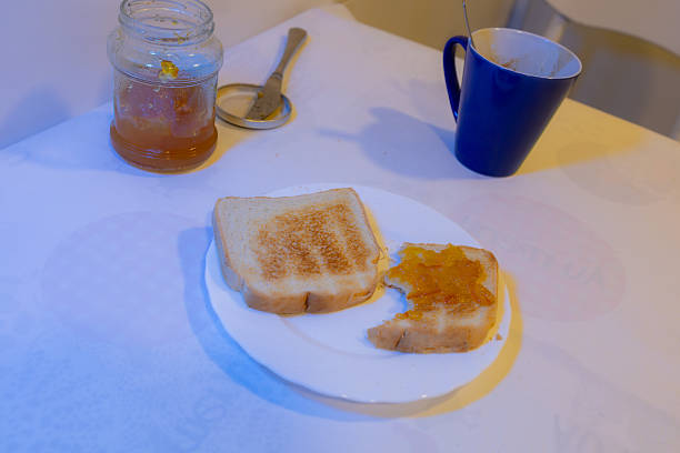 Toasted bread with orange marmalade served with coffee and open jar on light-colored table