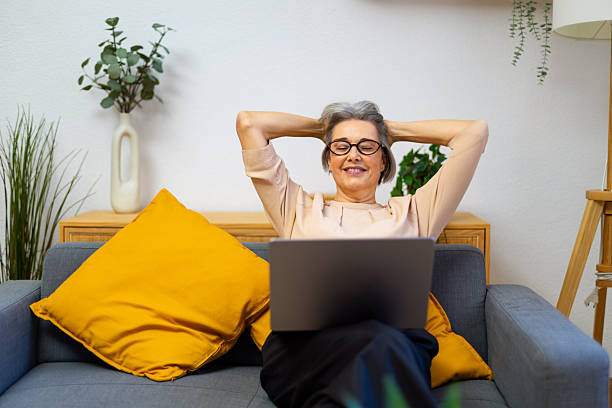 istock Mature woman relaxing hands behind head on sofa with laptop 2245214397