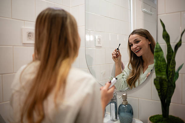 istock Woman smiling applying mascara in bathroom mirror 2245215113