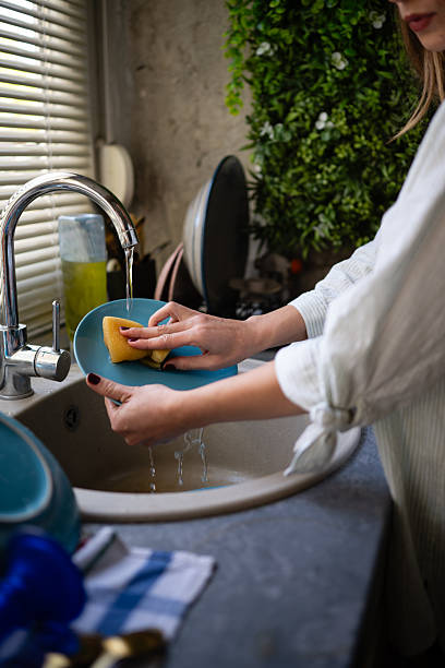 istock Woman washing dishes with sponge in kitchen sink 2245215540