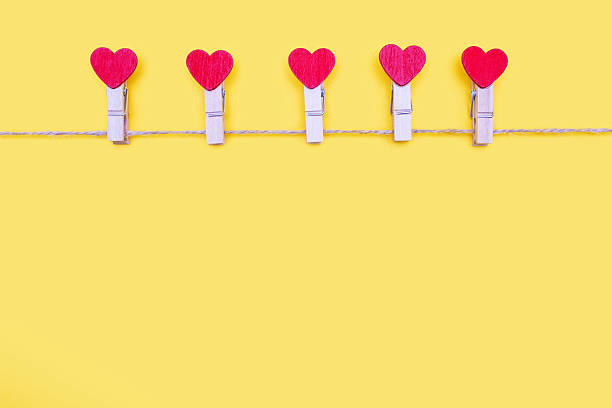 Clothespins decorated with hearts hang on a rope on a yellow background. Free space for text. Concept for lovers. Valentine's Day holiday. Decor in the form of clothespins and free space for items